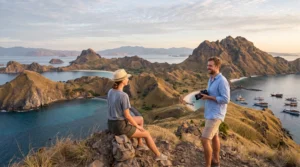 Two travellers on the Padar Island ridge above three curving bays at sunrise