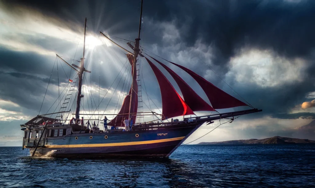 Ananda phinisi sailing under red sails in Komodo