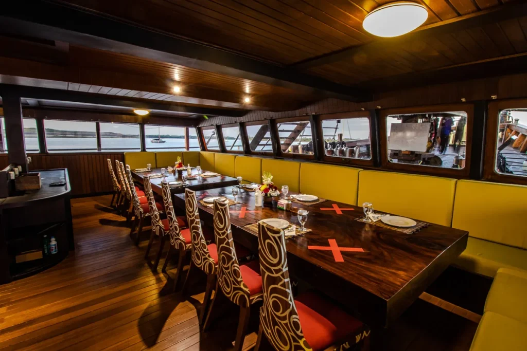 Long wooden dining table with carved high-back chairs and banquettes aboard Cheng Ho