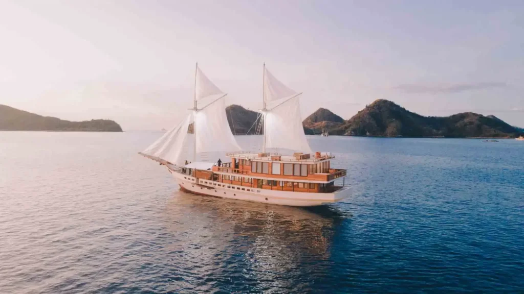 Elbark Cruise under white sails on calm water with rocky islands behind