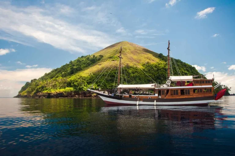 Side view of the Kira Kira phinisi at anchor with a forested hill behind