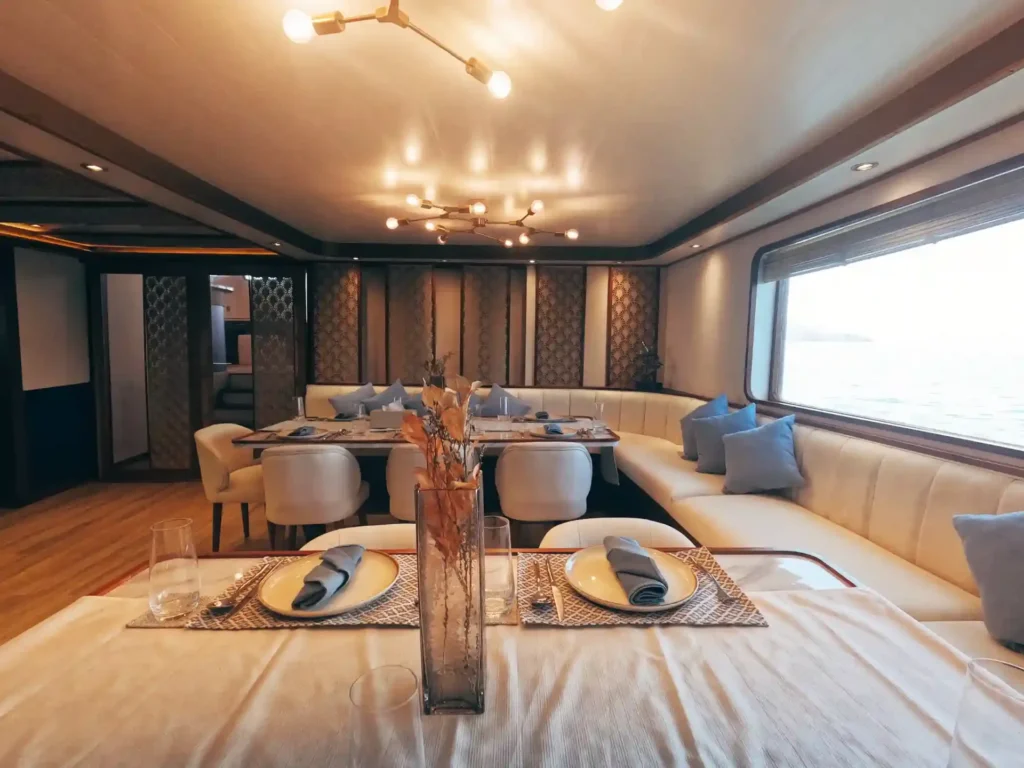 Dining table set with plates beside a cushioned lounge under a chandelier aboard Nayara Cruise