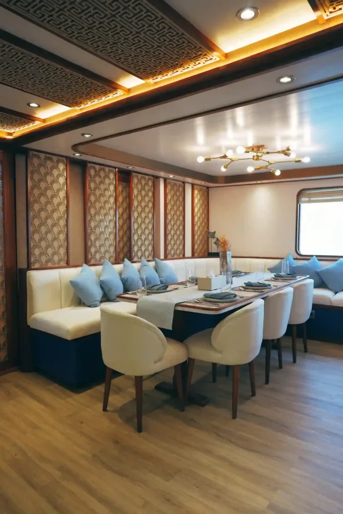 Dining table with white chairs and a cushioned banquette under a chandelier aboard Nayara Cruise