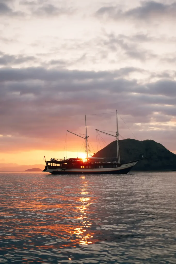 Nayara Cruise anchored at sunset beside a hilly island, the sun reflecting on the water