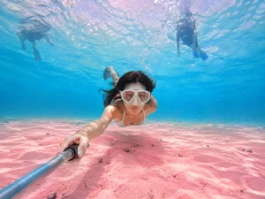 Woman taking an underwater selfie while snorkeling in crystal clear waters over pink sand during her private Komodo charter excursion