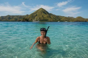 Tourist smiling while snorkeling in clear turquoise waters near Komodo Island on a 4-day boat tour from Lombok.