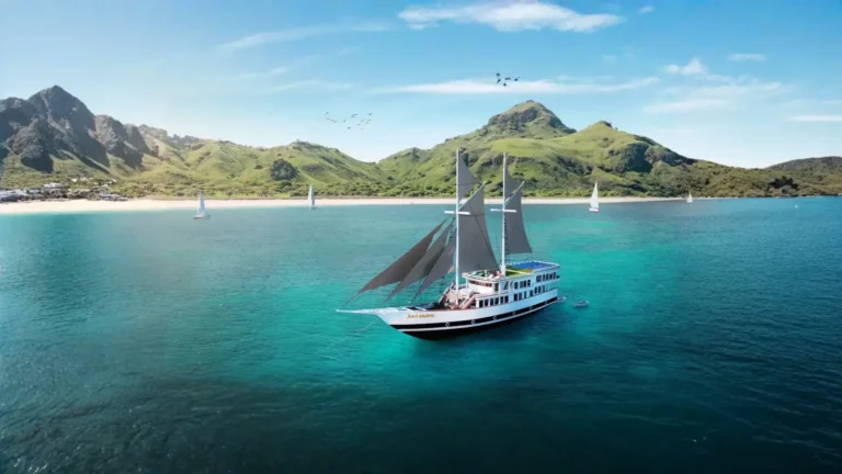 Sukha Sail 2 phinisi anchored in turquoise water below a green Komodo hillside