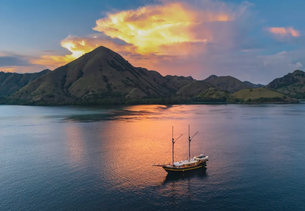 Ta’Talasa expedition phinisi cruising beneath volcanic hills in Komodo