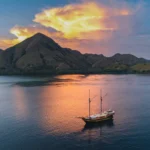 Ta’Talasa expedition phinisi cruising beneath volcanic hills in Komodo