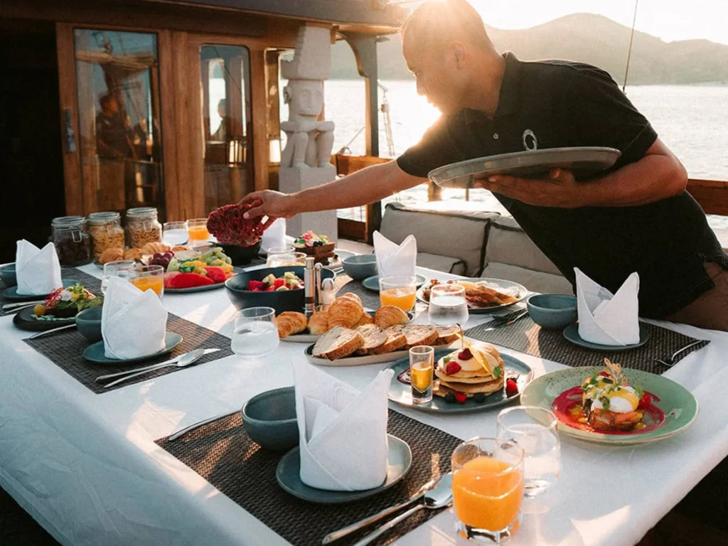 Crew serving breakfast at the outdoor dining table aboard The Oracle