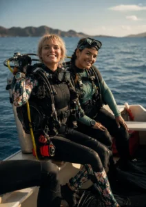 Two female scuba divers in full gear smiling on the edge of a small boat, getting ready to dive into the Komodo waters.
