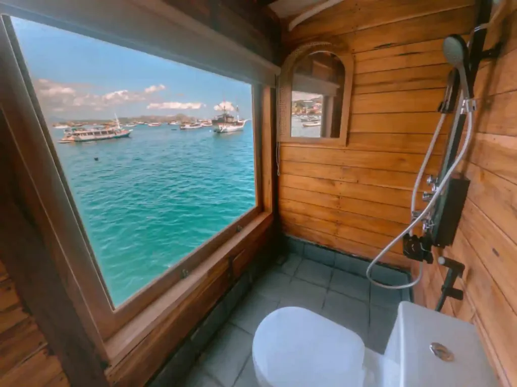 Cabin bathroom with shower, toilet and a large window onto the bay aboard Yumana