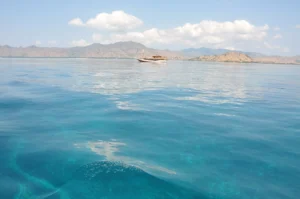 Calm turquoise shallows with a boat and low islands on the horizon