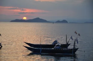 Outrigger boats silhouetted as the sun sets over islands off Labuan Bajo