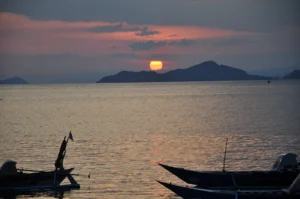 Setting sun behind islands with outrigger boats in Labuan Bajo bay