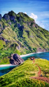 Hikers on the green ridge trail above a turquoise bay on Padar Island