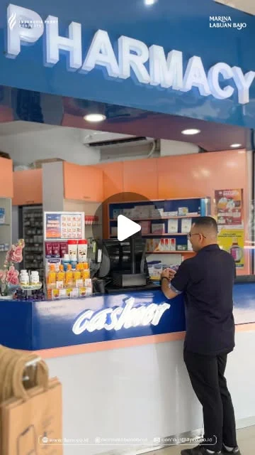 Customer standing at a pharmacy service counter below a blue pharmacy sign