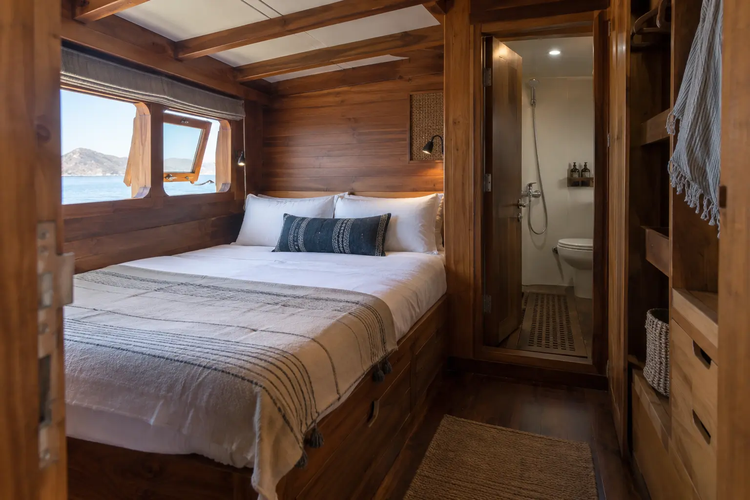 A teak liveaboard cabin with a double bed, storage, window and compact ensuite bathroom.