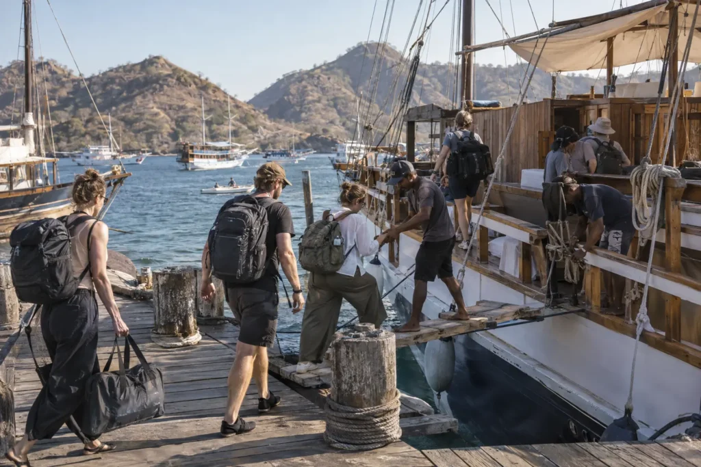 Travelers board a shared Komodo phinisi with crew assistance at Labuan Bajo harbor.