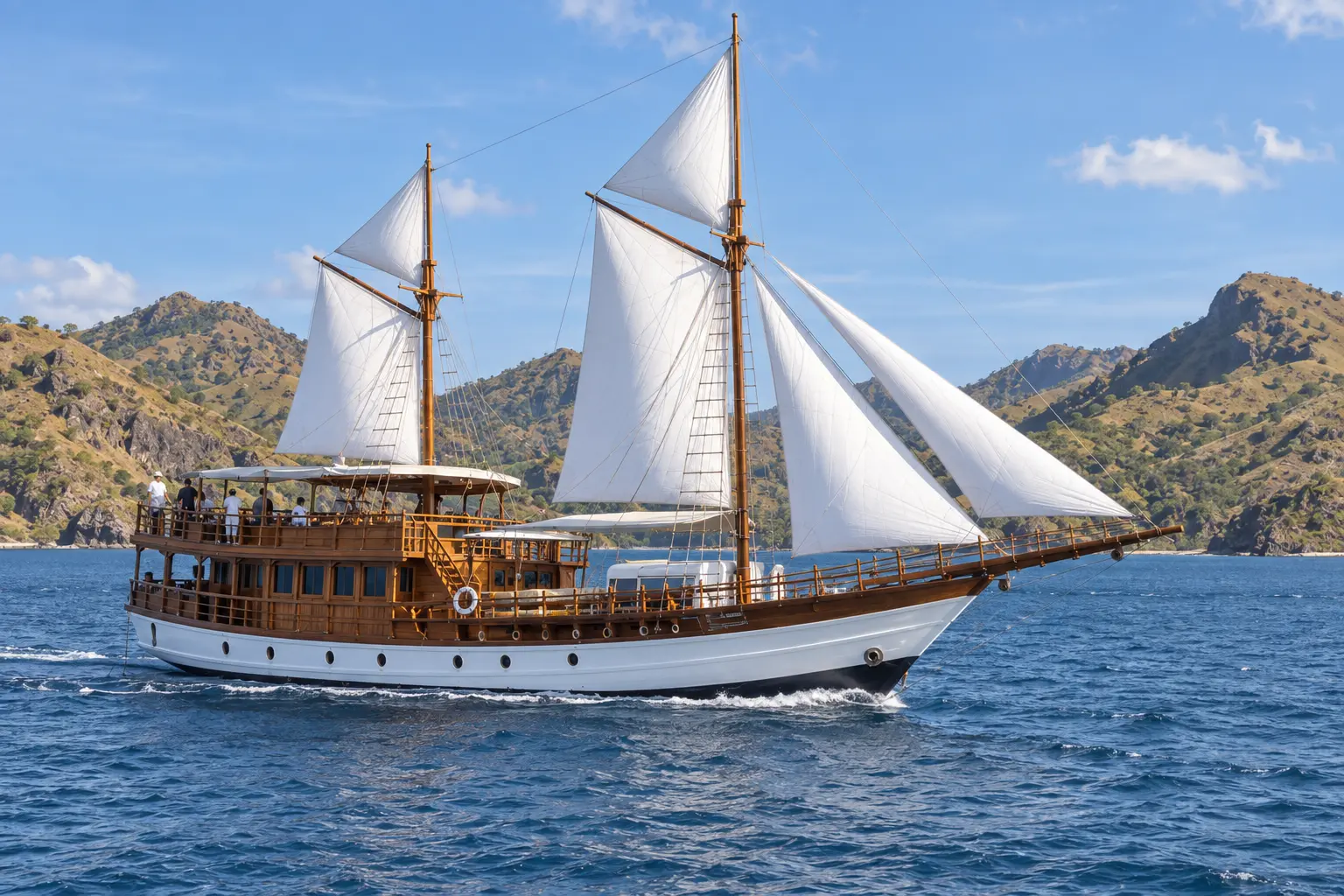 Luxury phinisi sailing between dry green-gold islands in Komodo National Park