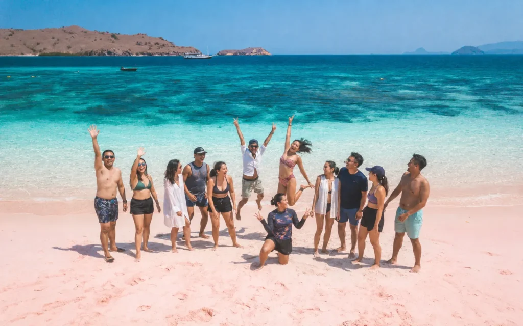 Group of travellers standing on Pink Beach beside turquoise water in Komodo National Park