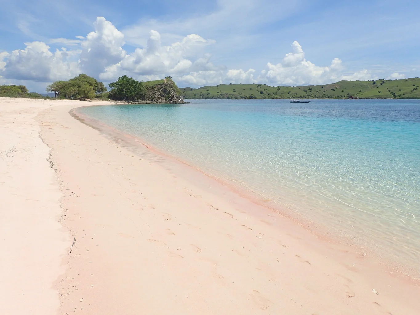 Pale pink sand borders turquoise water beneath coastal hills.