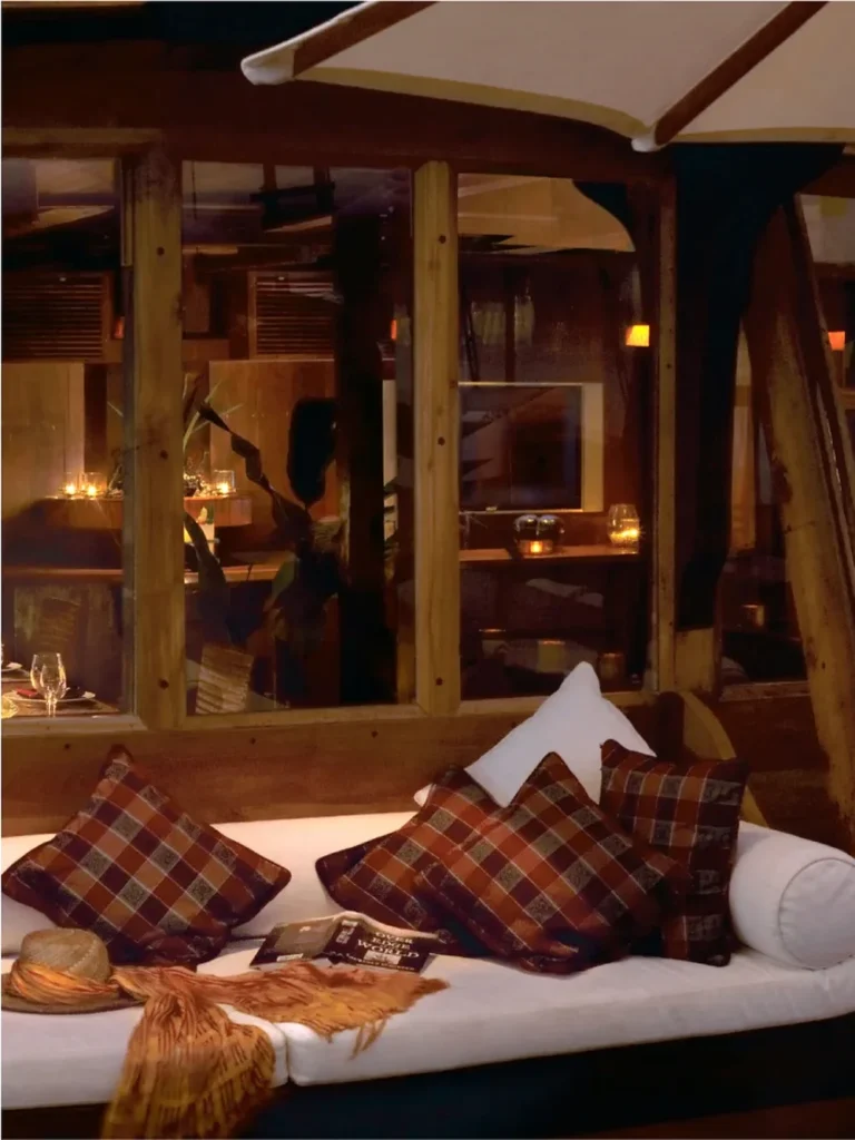 Teak saloon daybed with tartan cushions and warm lamp light aboard Silolona
