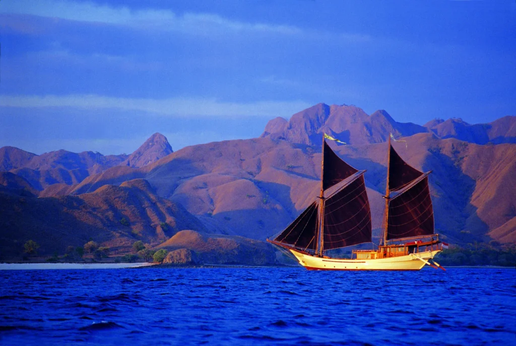Silolona under dark sails on blue water near rugged islands
