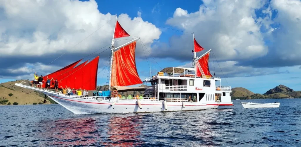 Thalassa one phinisi side profile with red sails in Komodo waters